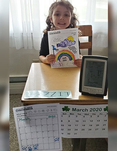 Girl holding coloring page at desk with weather display