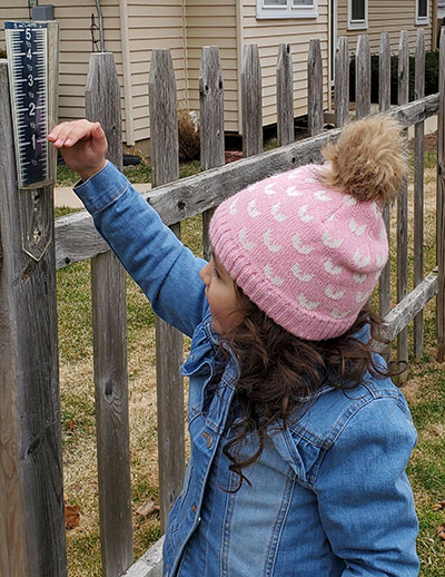 Girl checking rain gauge on fence