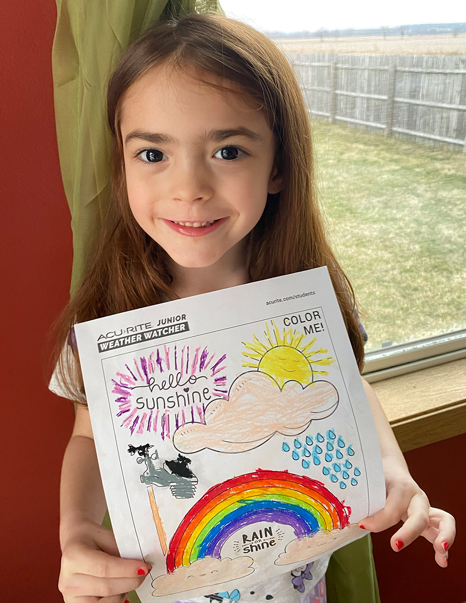 Girl holding coloring page in front of window